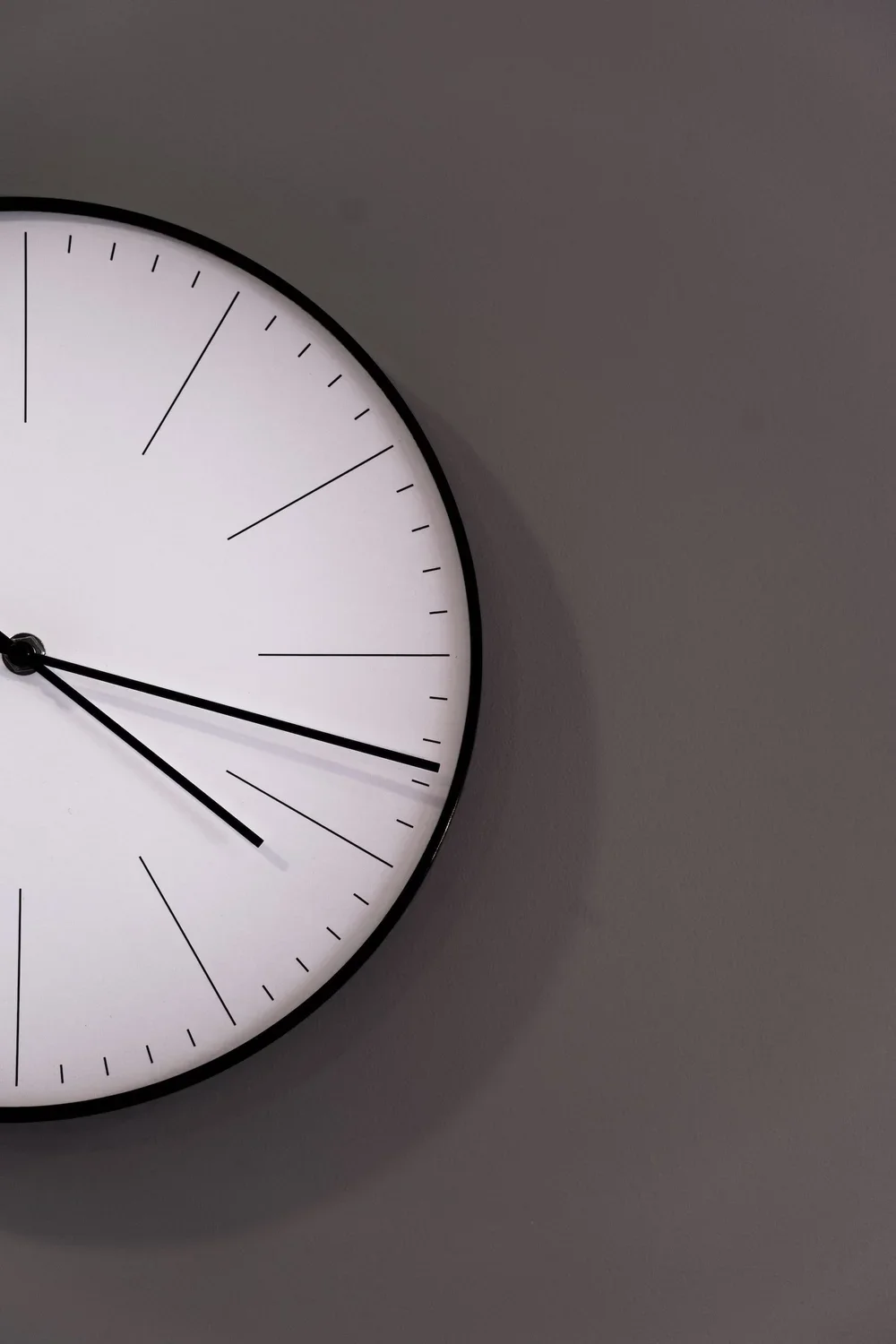Close-up of a modern wall clock showing approximately 4:15 time on a gray wall.