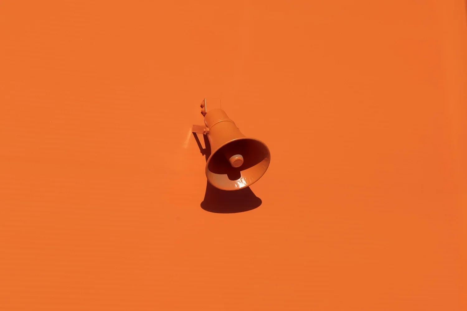 An orange wall with a mounted orange loudspeaker.
