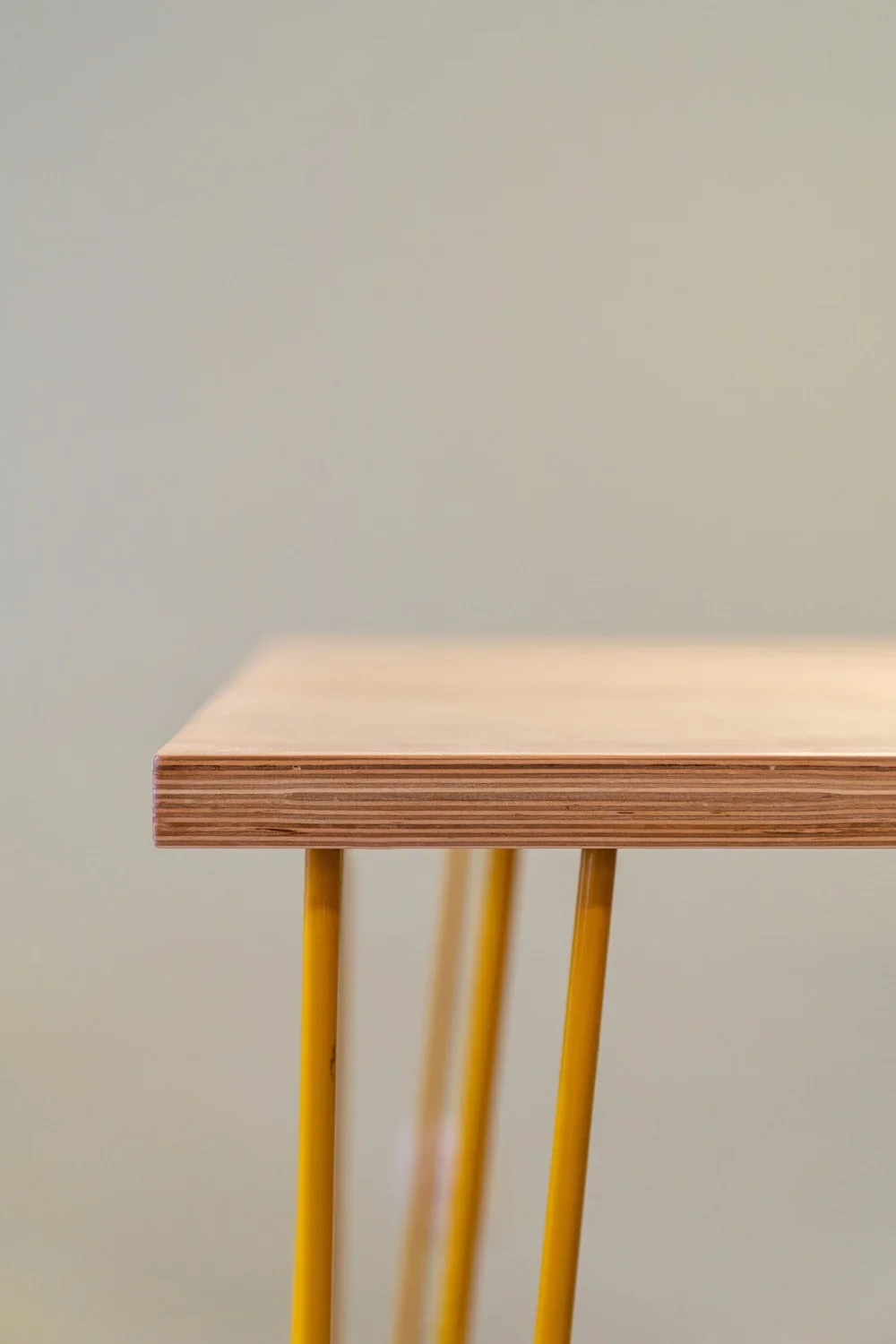 Close-up of a wooden table with yellow metal legs against a plain, pale background.