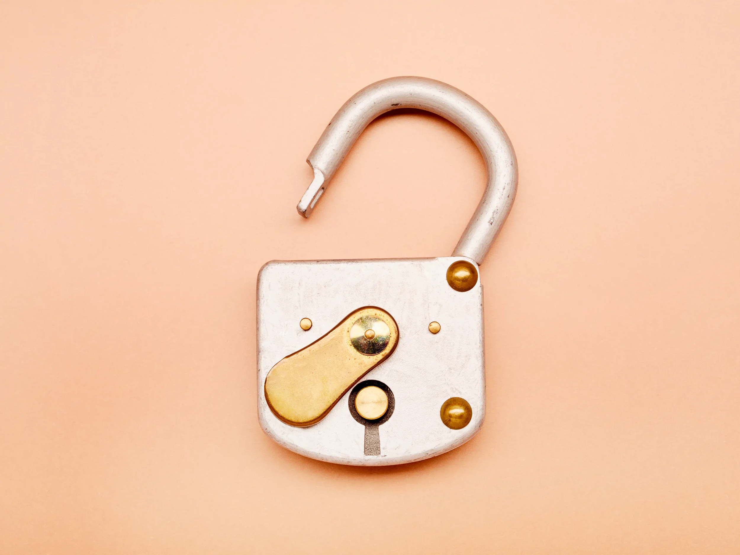 Close-up of a broken or partially disassembled silver and gold-colored mechanical lock or latch on a light pink background.