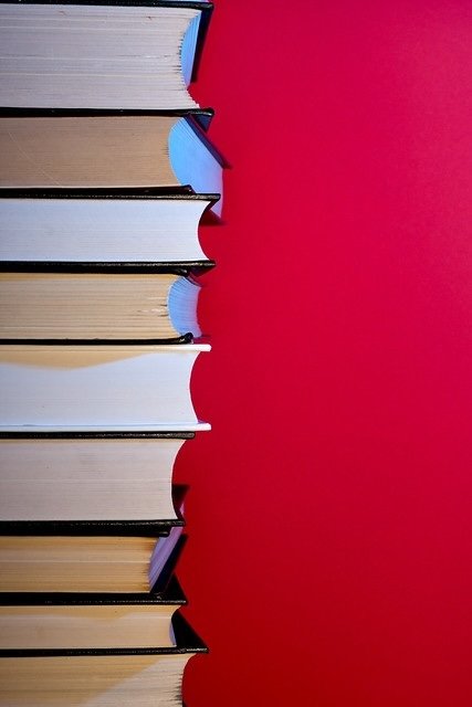 Stack of books leaning against a bright pink wall