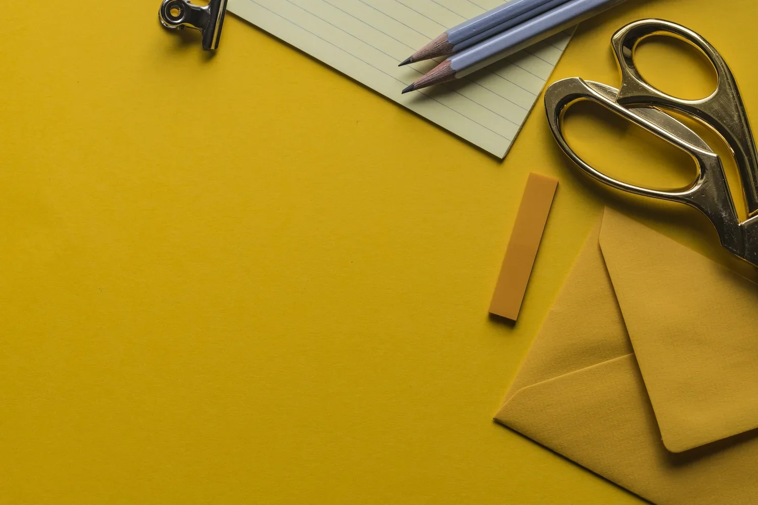 Yellow desk with notebooks, colored pencils, scissors, and paper clips.