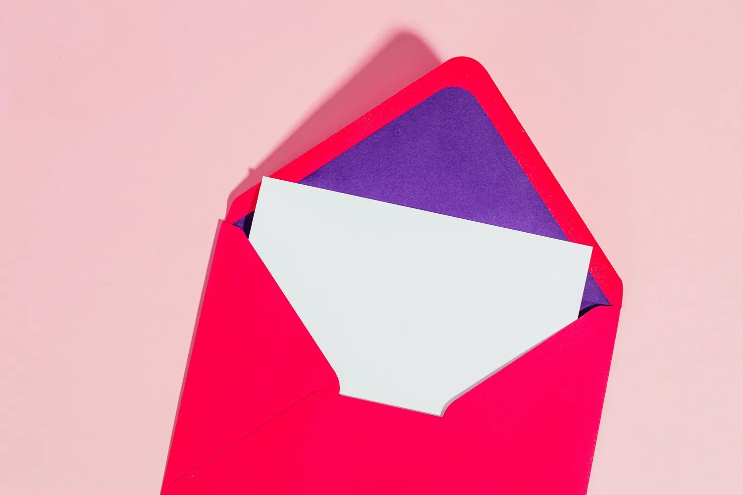 A red envelope holding a purple card and a white card inside, on a pink background.